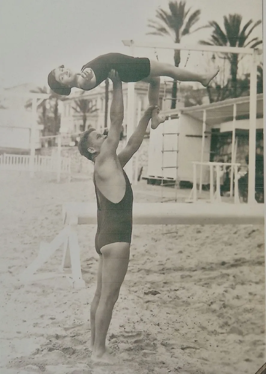 Iza faisant de la gymnastique sur la plage, portée à bout de bras